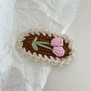 Detailed knit texture of a brown crochet clip with a pink tulip and white wave borders