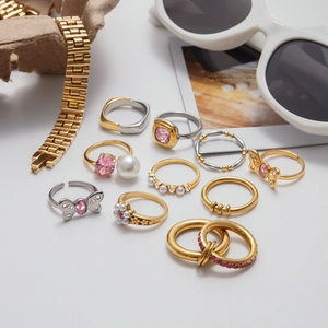 Flat lay of pink zircon rings with golden butterfly and pearl details on grey surface