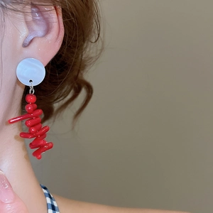 Close-up of red resin coral branch earrings with white mother-of-pearl stud on model's ear