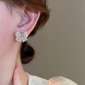 Macro detail of bowknot stud earrings with pearls and crystals on a model ear