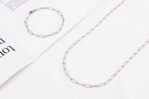 Detailed close-up of a silver-tone safety pin chain necklace and bracelet set on a magazine