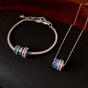 Macro shot of silver bangle and necklace set with blue gemstone rolling pendants