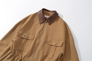 Detailansicht der khakifarbenen Jacke mit braunem Lederkragen und Kreuz-Reißverschluss