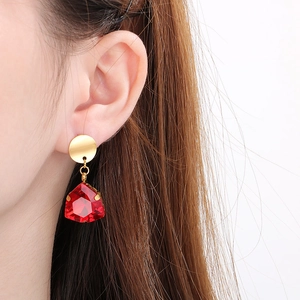 Close-up of a large faceted red crystal drop earring with golden hook on a model