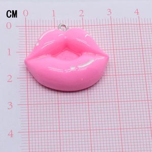 Pink resin lip pendant charm with metal ring measured on a scale mat for size reference