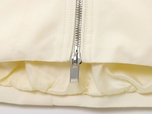 Detail of off-white bomber jacket featuring a silver metal zipper and ribbed windproof hem