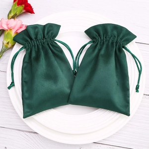 Dark green velvet jewelry pouches with drawstring on white ceramic plate and wooden background