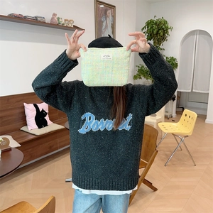 Detail of a light green knitted cosmetic bag held against a grey embroidered sweater
