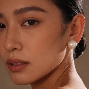 Elegant woman wearing a large cream white faux pearl stud earring in a high-end close-up view