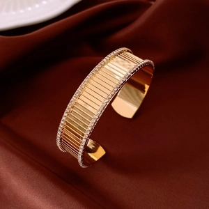 Dettaglio di bracciale rigido dorato con pavé di cristalli e strisce testurizzate
