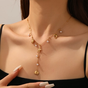 Detail of gold Y-chain necklace featuring starfish, shell pendants and pearls on a model