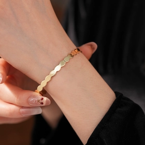 Detail view of a gold wavy textured metal cuff bracelet worn on a female wrist