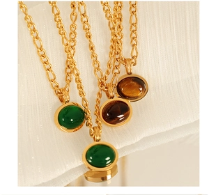 Dettaglio di collane in oro con pendenti in pietra ovale verde e marrone su tessuto bianco