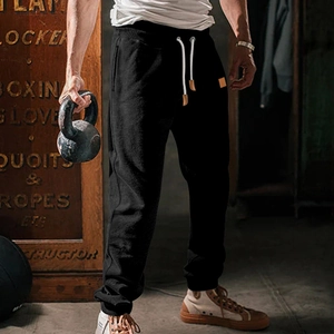 Detail of men's black sweatpants featuring white drawstring with brown leather tips