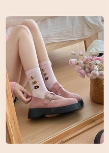 Close-up of pink knit socks with bear patterns paired with Mary Jane shoes on wood floor
