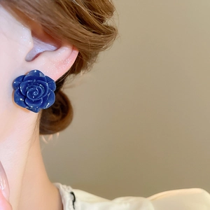 Gros plan de boucles d'oreilles roses bleu foncé portées avec détails de texture florale