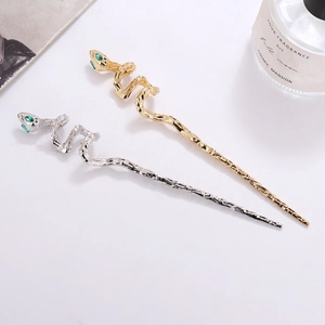 Snake hairpins in gold and silver finish with sparkling green gemstone eyes on white surface
