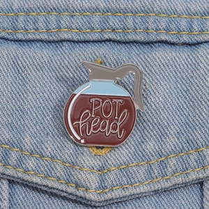 Detail of coffee pot enamel pin with POT head text on blue denim fabric