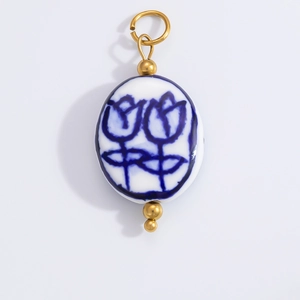 Detailed view of white ceramic bead charm with blue tulip pattern and gold metal accents