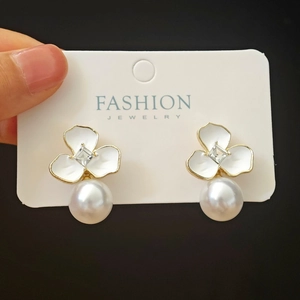 Close-up of gold floral earrings with white enamel petals, square zircon, and large pearl