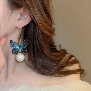Detail view of a long butterfly drop earring with a blue bow and a large white pearl