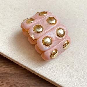 Close-up of pink marble resin bracelet with gold dome studs on a textured fabric