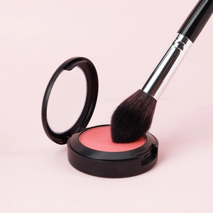 Coral pink blush powder in black compact with soft makeup brush application detail