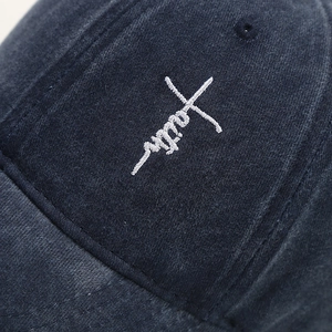 Detailed close-up of white 'faith' cross embroidery on a navy washed cotton baseball cap