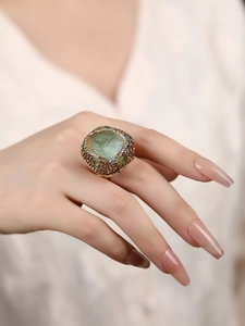 Detail of a large light green raw gemstone ring with pavé crystals on a model hand