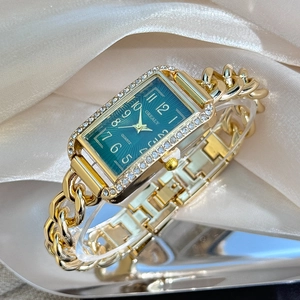 Macro view of women's gold rectangular watch with emerald dial and rhinestone accents