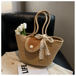 Detail of straw tote bag with brown leather flap, pearl buckle and lace bow on sofa