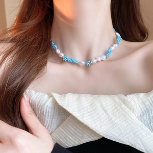 Detail view of pearl and blue flower necklace worn on neck highlighting glossy finish