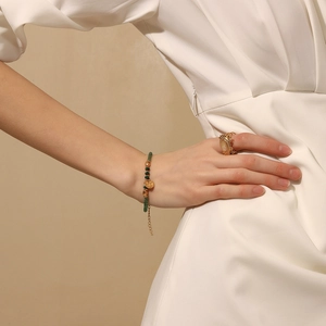 Detailed view of green beaded bracelet with gold disk and vintage oval ring on hand