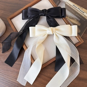 Dettaglio di grandi fermagli per capelli a fiocco in chiffon nero e crema su vassoio
