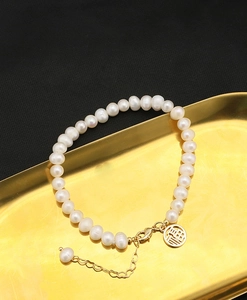 Detail of natural pearl bracelet with gold Fu charm on an elegant metal tray