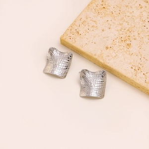 Macro shot of silver square textured earrings placed on stone showcasing minimalist design