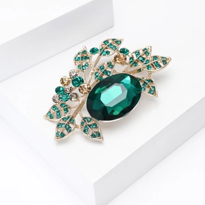 Macro detail of vintage gold-tone leaf brooch with green and champagne crystals