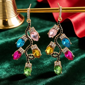 Macro detail of colorful Christmas bulb earrings with rhinestones on green velvet