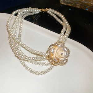 Macro shot of multi-layer white pearl necklace with gold camellia floral pendant detail