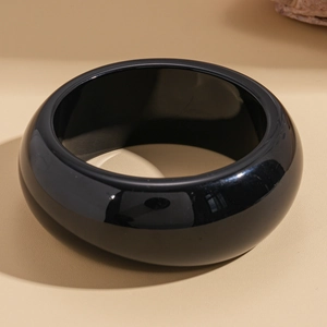 Detailed view of a wide thick-walled black resin bangle with a polished mirror finish