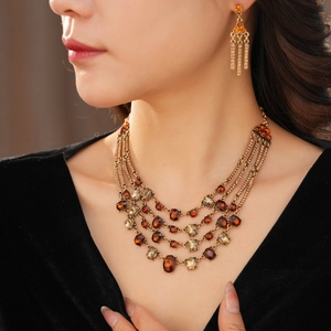 Close-up of vintage layered gold necklace and tassel earrings with amber crystal detail