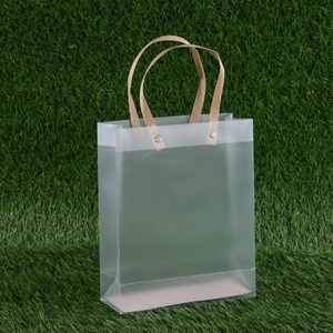 Frosted transparent gift bag with beige ribbon handles on green grass, durable PP material