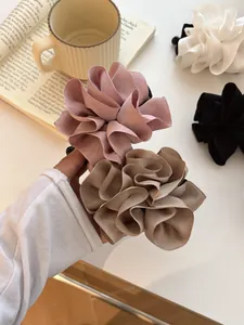 Détail macro d'une pince à cheveux fleur en satin plissé aux tons rose, crème et noir soyeux
