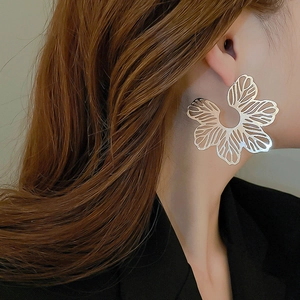 Macro shot of large silver hollow petal earrings on model with black suit and brown hair