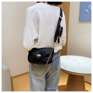 Close-up of black quilted leather crossbody bag with gold chain and wide woven strap