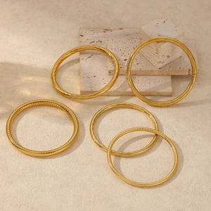 Set of 5 gold minimalist stainless steel textured bangles on a stone pedestal display