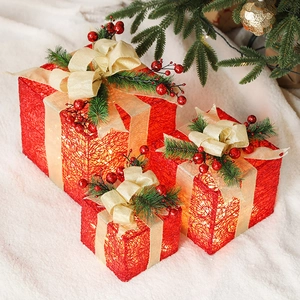 Three-piece glowing red Christmas gift boxes with gold bows and pine cone decorations