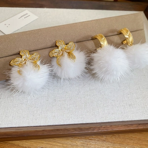 Detail of gold flower earrings and hoops with white fur balls on a display card