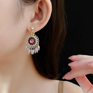 Ethnic style gold-tone earrings with pink crystal centers and grey bead tassels on model