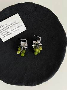 Close-up of C-shaped grape cluster earrings with green crystals on a black tray